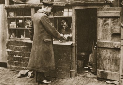 Een schoenmaker, gevestigd in een geïmproviseerde kraam in een geplaveide Mayfair steeg, neemt laarzen aan van een chauffeur, uit Wonderful London, gepubliceerd 1926-27 door English Photographer